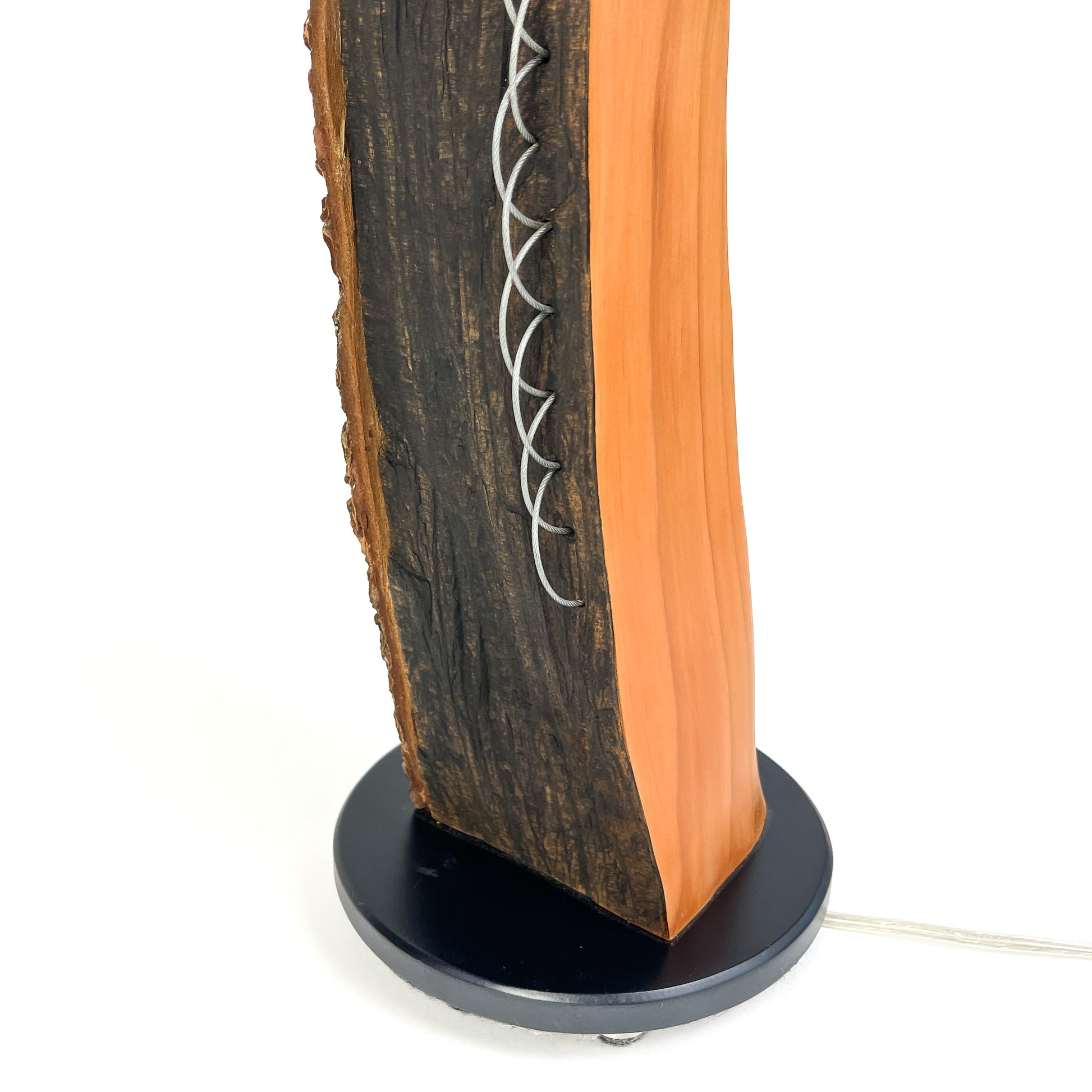 Close-up of a lamp base: dark wood with bark texture and metal string detail.