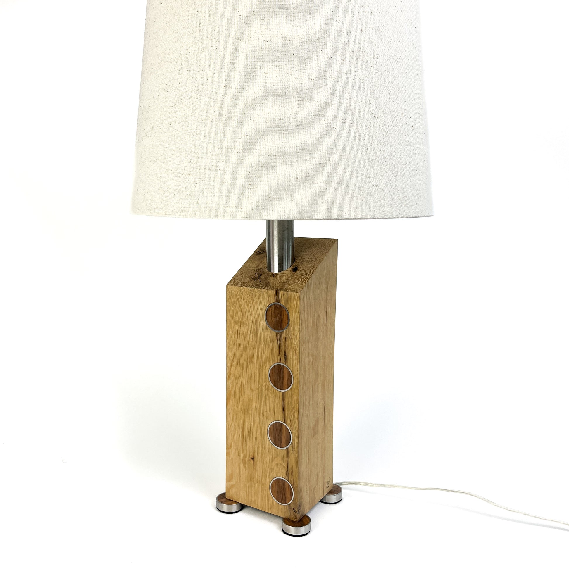 A table lamp with a light wood base, metal circles, white shade, and small metal feet.