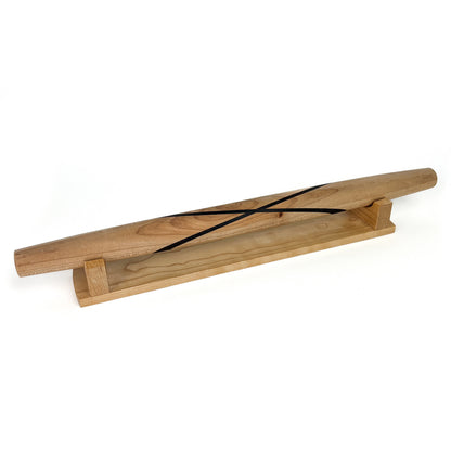 A light-colored wooden French rolling pin with two thin dark stripes, resting on a wooden stand. The pin has a smooth, polished finish.