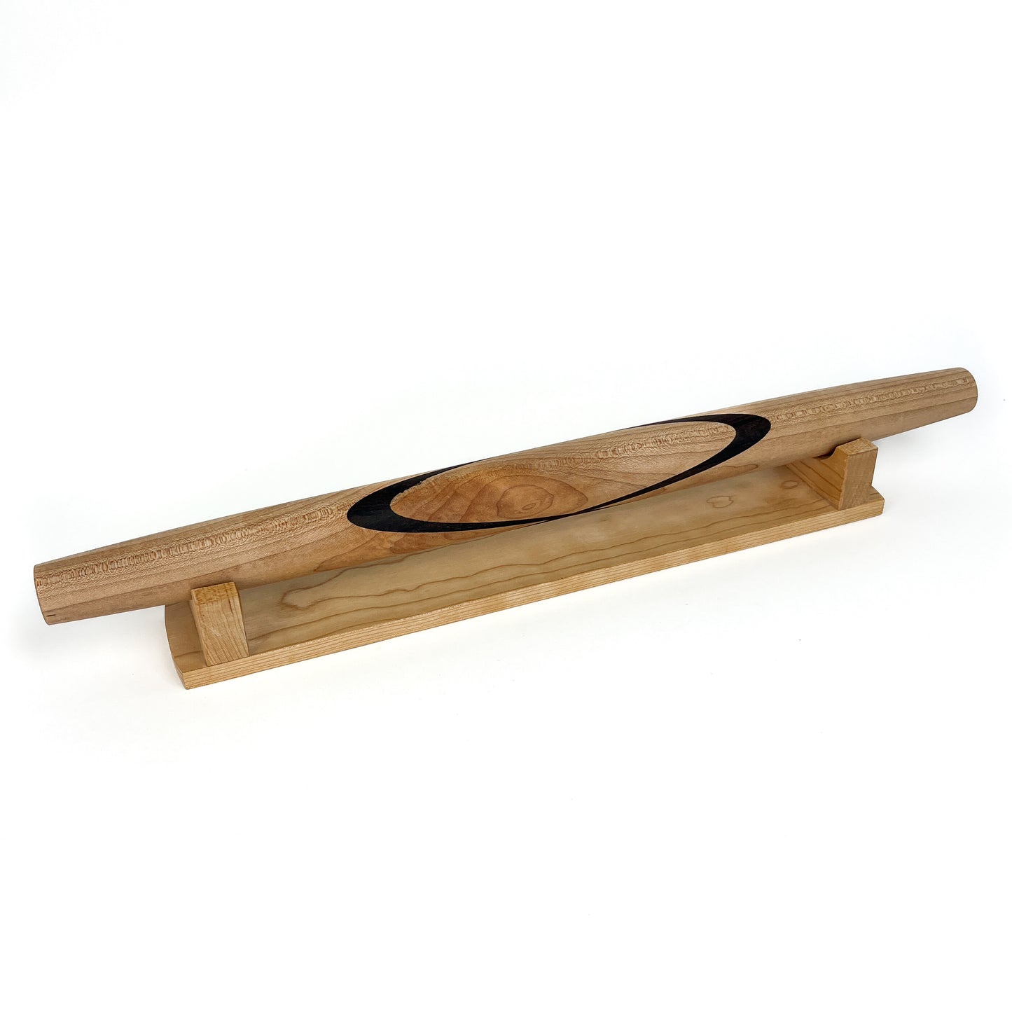 A Sugar Maple French rolling pin with a Black Walnut Celtic knot inlay, resting on a wooden stand. The pin has a smooth finish.