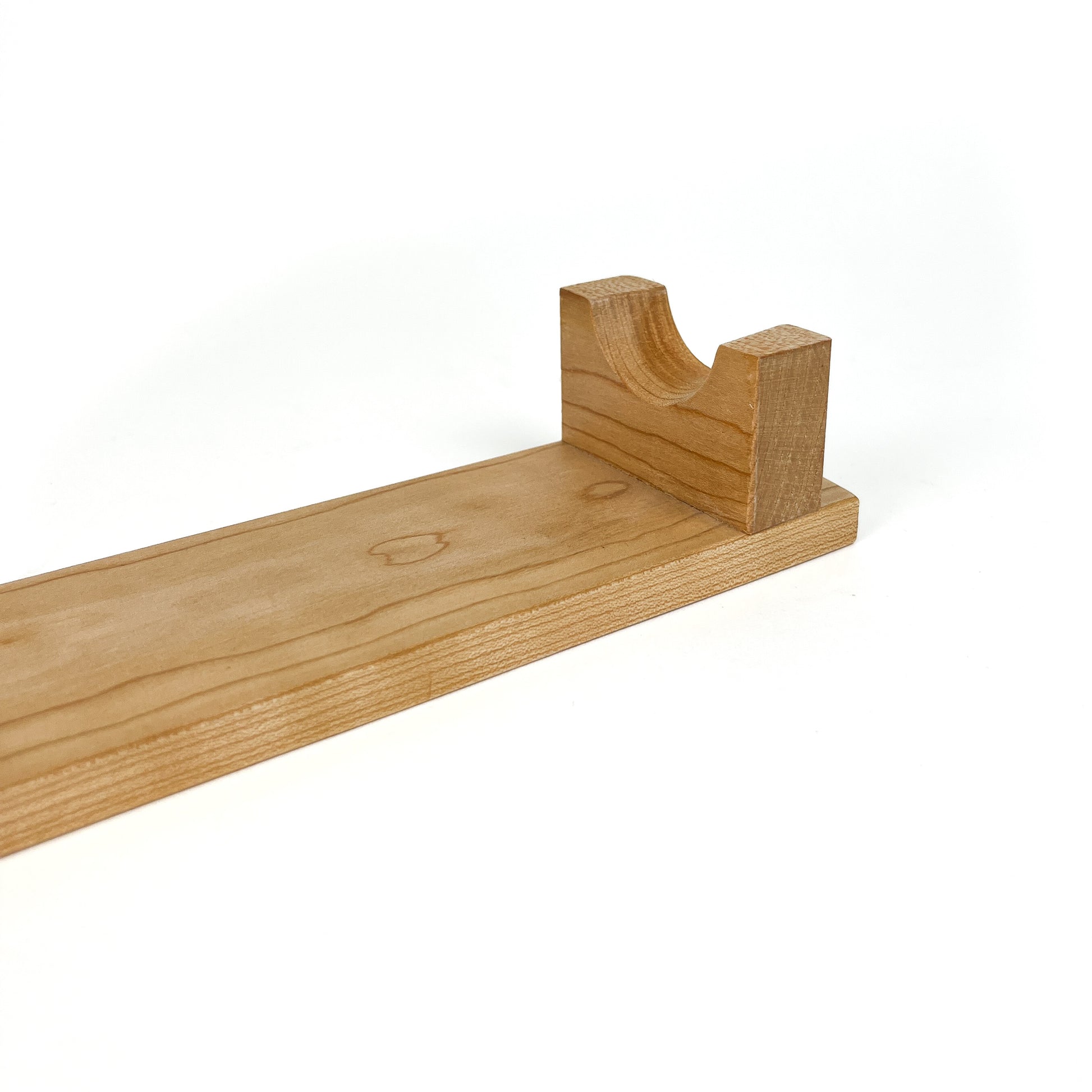 A close-up of a light wooden French rolling pin stand, showing one of the carved supports. The stand has a visible wood grain.