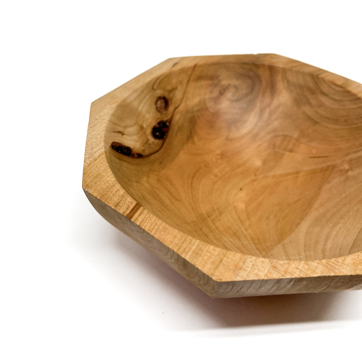 A close-up of a light-colored, eight-sided wooden bowl with visible grain and a smooth, carved interior. The bowl has a shallow depth.