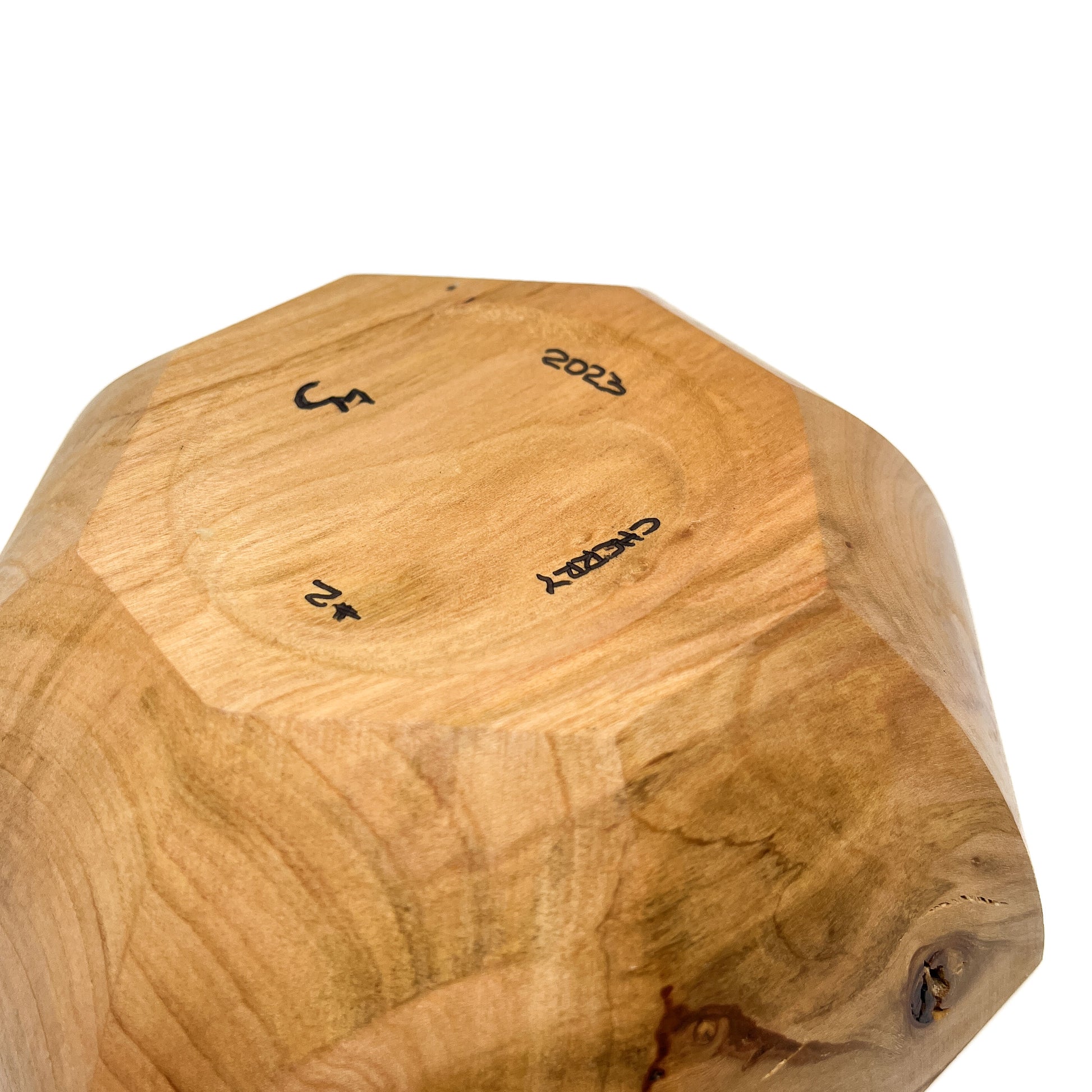 A close-up of the bottom of a light-colored, eight-sided wooden bowl with markings.
