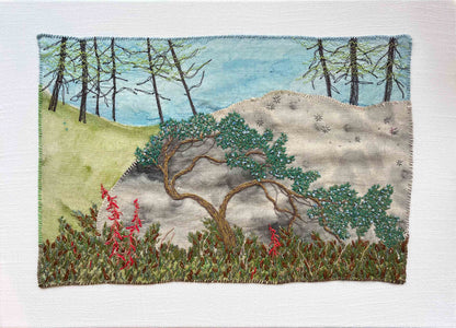 Embroidered wall art: crooked tree on a rocky hill, tall trees in the back, and red flowers in the front.
