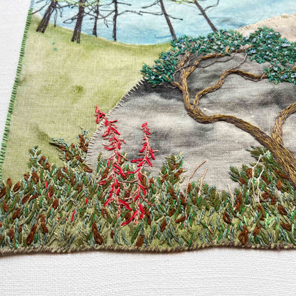 Close-up of embroidered wall art: bent tree, tall trees in the distance, and red flowers in a green foliage patch.