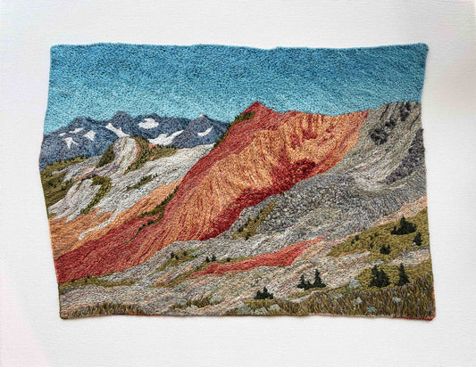 Embroidered wall art: mountain landscape with textured slopes, snow-capped peaks, and small trees.
