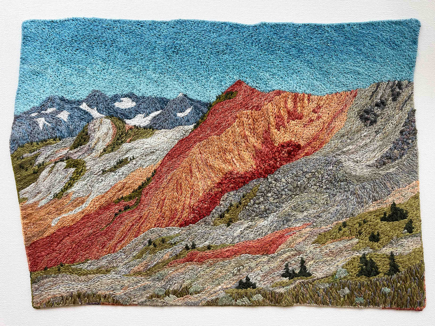 Embroidered wall art: mountain landscape with textured slopes, snow-capped peaks, and small trees.