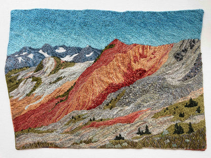 Embroidered wall art: mountain landscape with textured slopes, snow-capped peaks, and small trees.