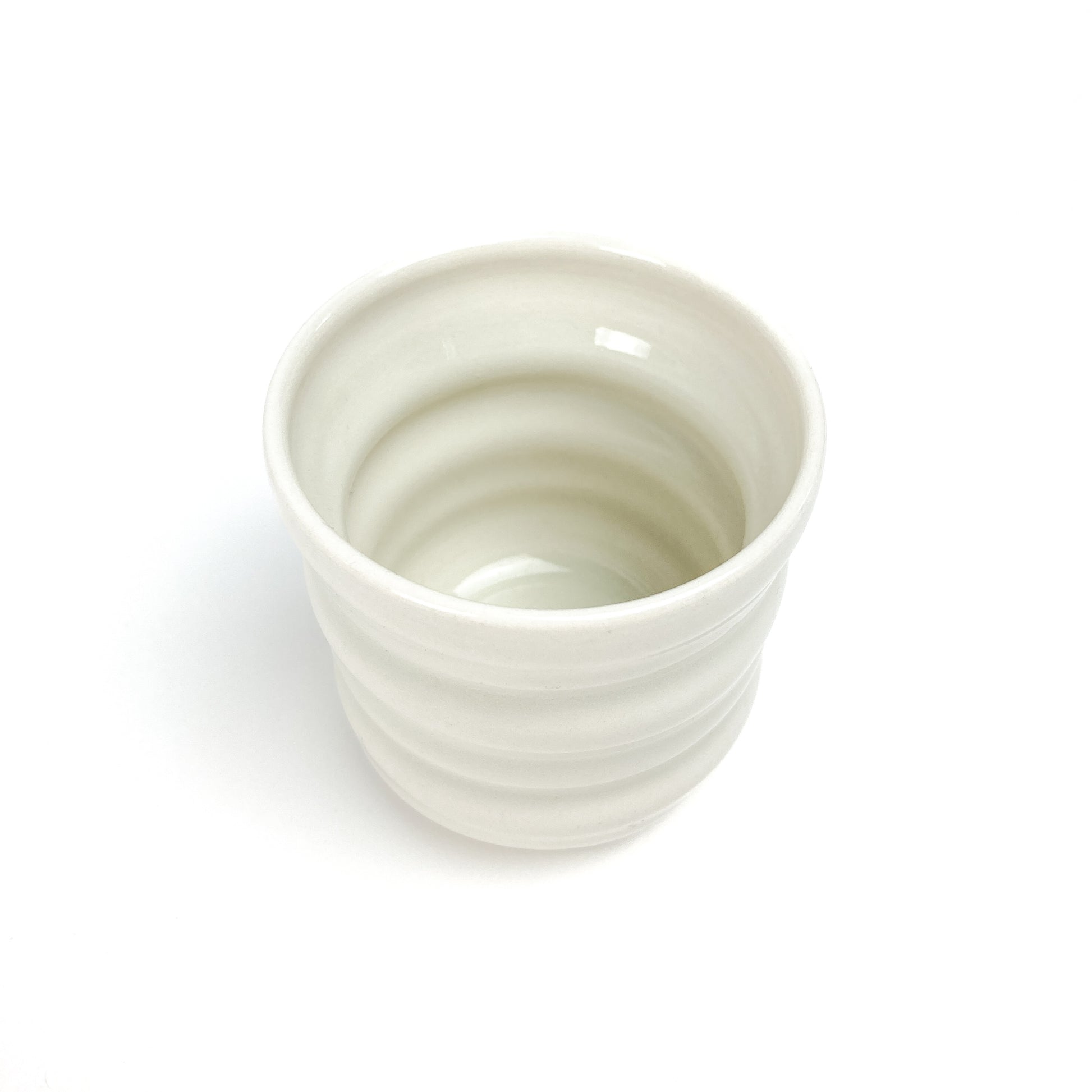 Top-down view of a small ceramic Yunomi cup with subtle horizontal ridges, showing its smooth, hollow interior.