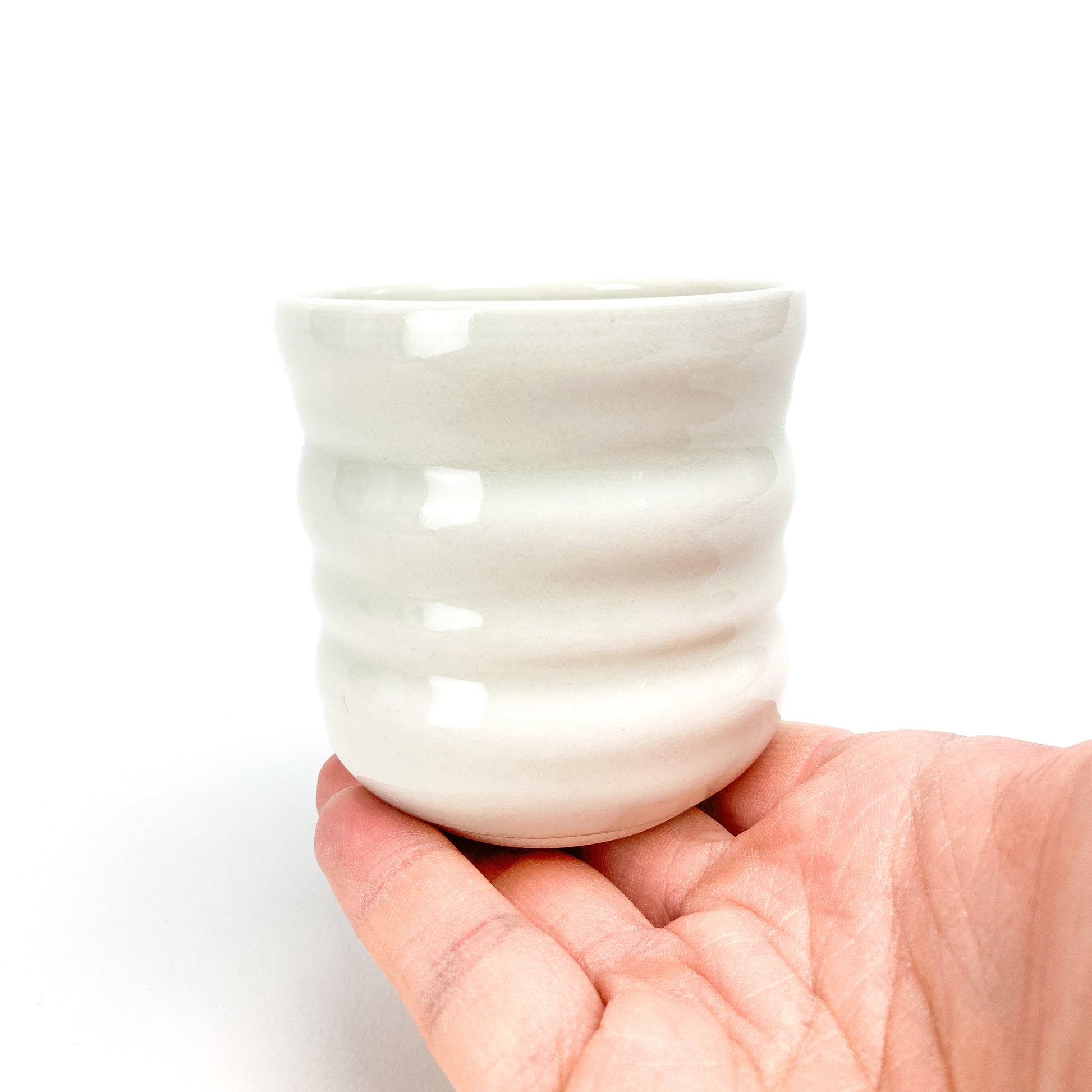 A small ceramic Yunomi cup with subtle horizontal ridges held in a person's open palm.