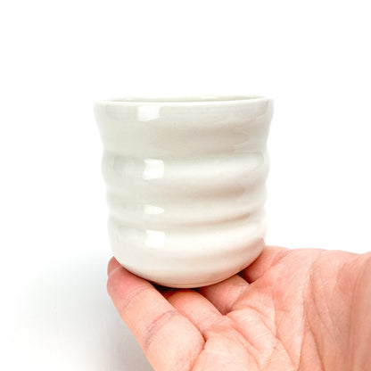 A small ceramic Yunomi cup with subtle horizontal ridges held in a person's open palm.
