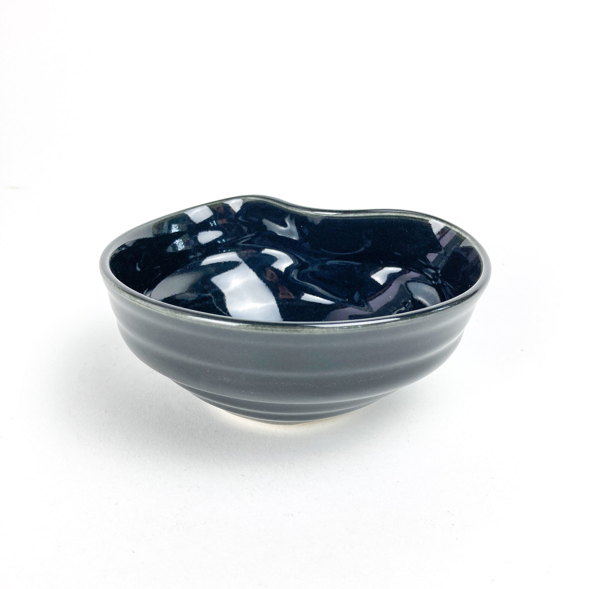 A small, dark, glossy ceramic concave bowl with subtle horizontal ridges on its exterior.