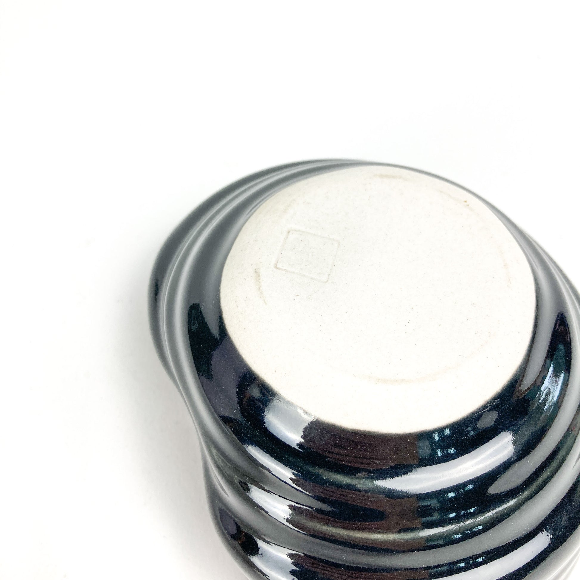 Bottom view of a small, dark, glossy ceramic bowl with textured, swirling ridges and a light-toned base with a square mark.