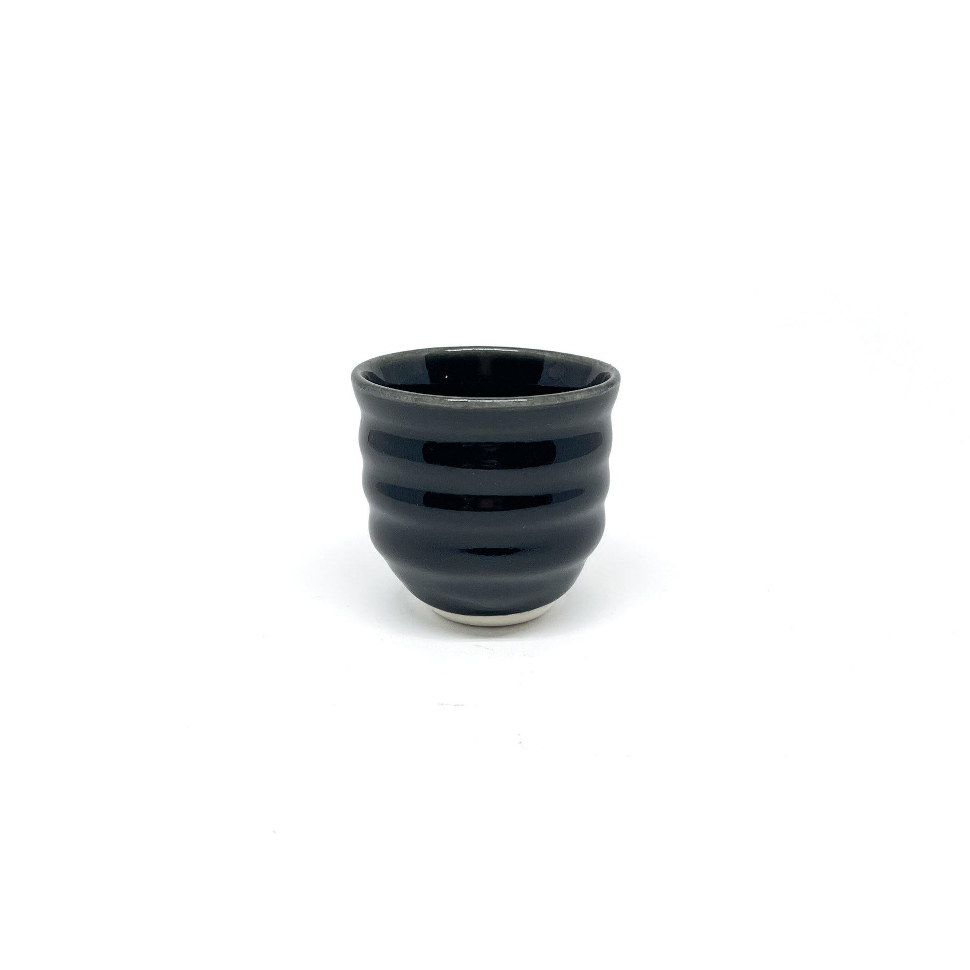 A small, dark ceramic Yunomi cup with horizontal ridges around its body and a lighter base.