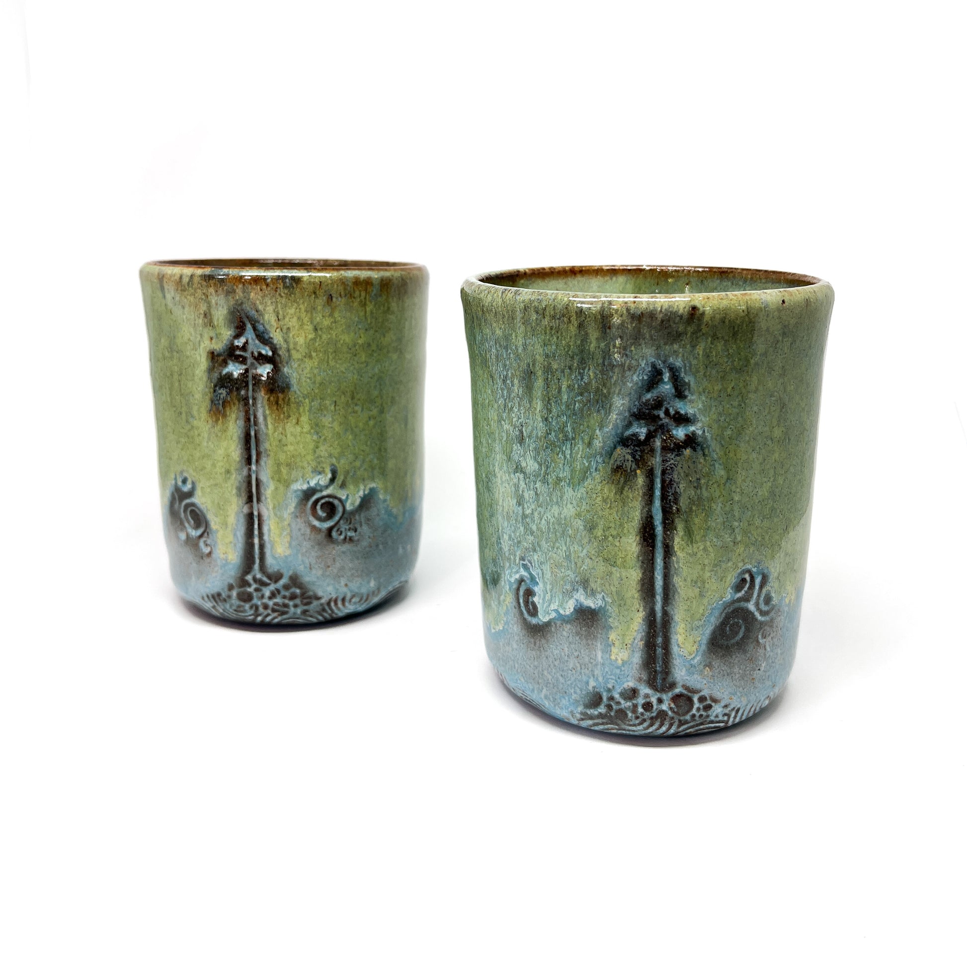 Two glazed terracotta cups with tree designs, isolated on white.
