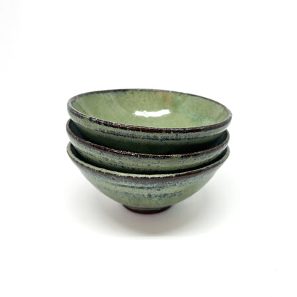 Stack of three green glazed terracotta bowls with dark rims.