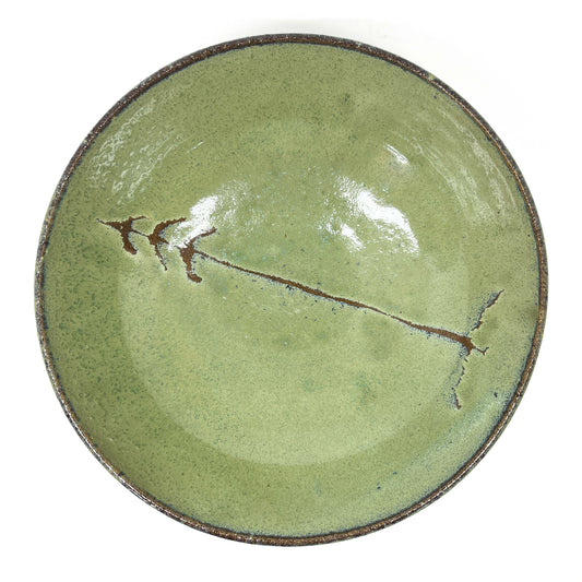 Green glazed terracotta plate with a tree design in the center, top-down view on a white background.
