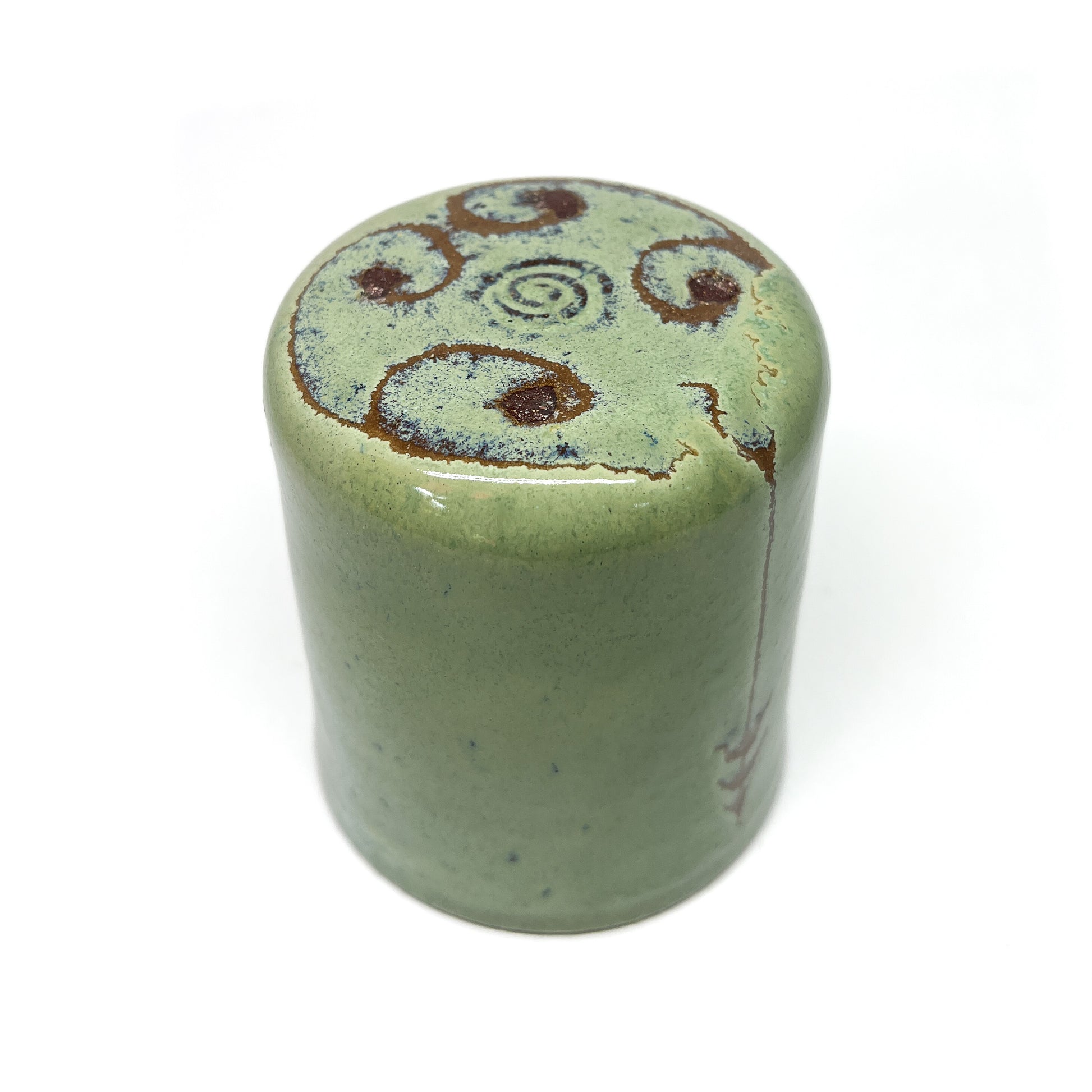 Green ceramic cup with brown spiral designs on top, angled view on a white background.