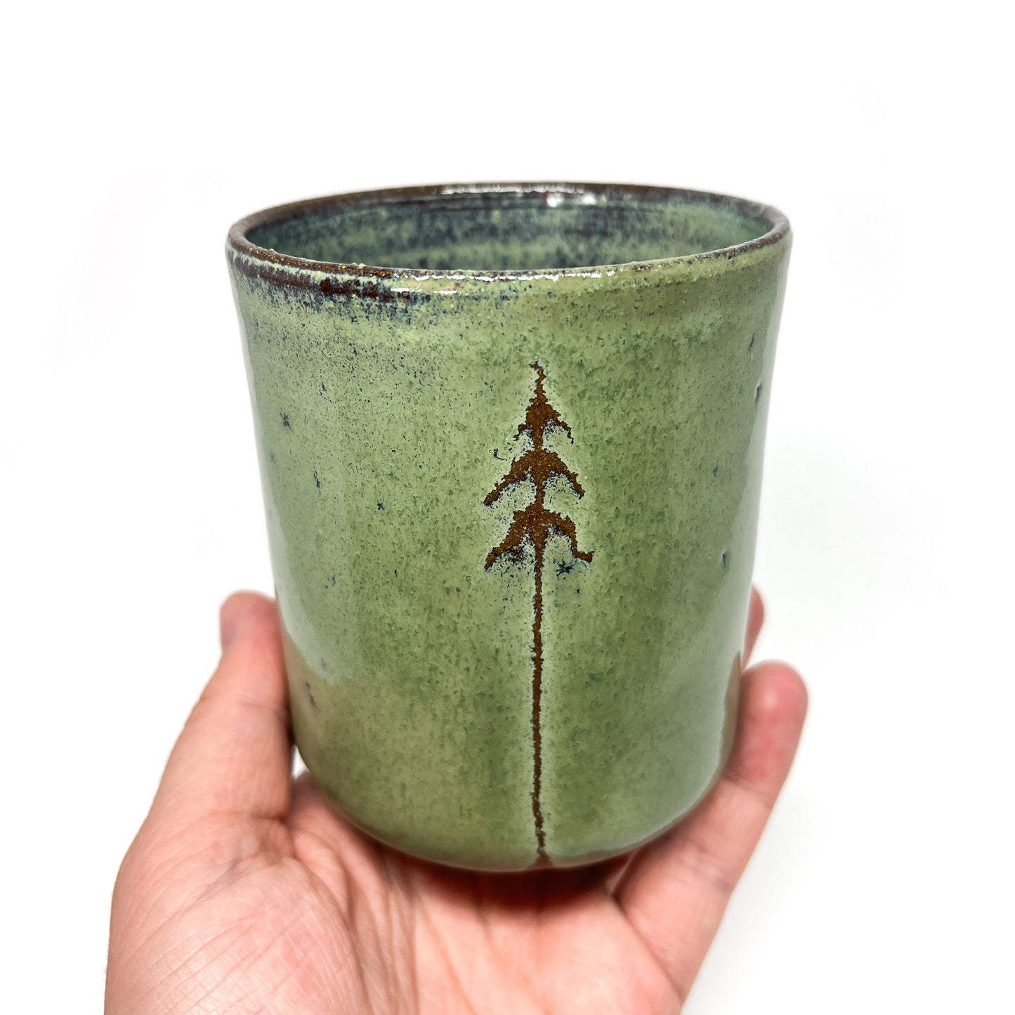 Hand holding a green ceramic cup with a tree design, isolated on white.