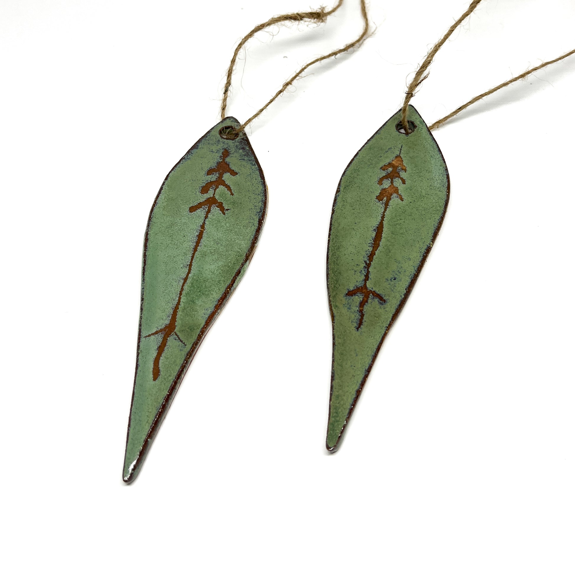 Two green leaf-shaped ornaments with tree designs and twine.