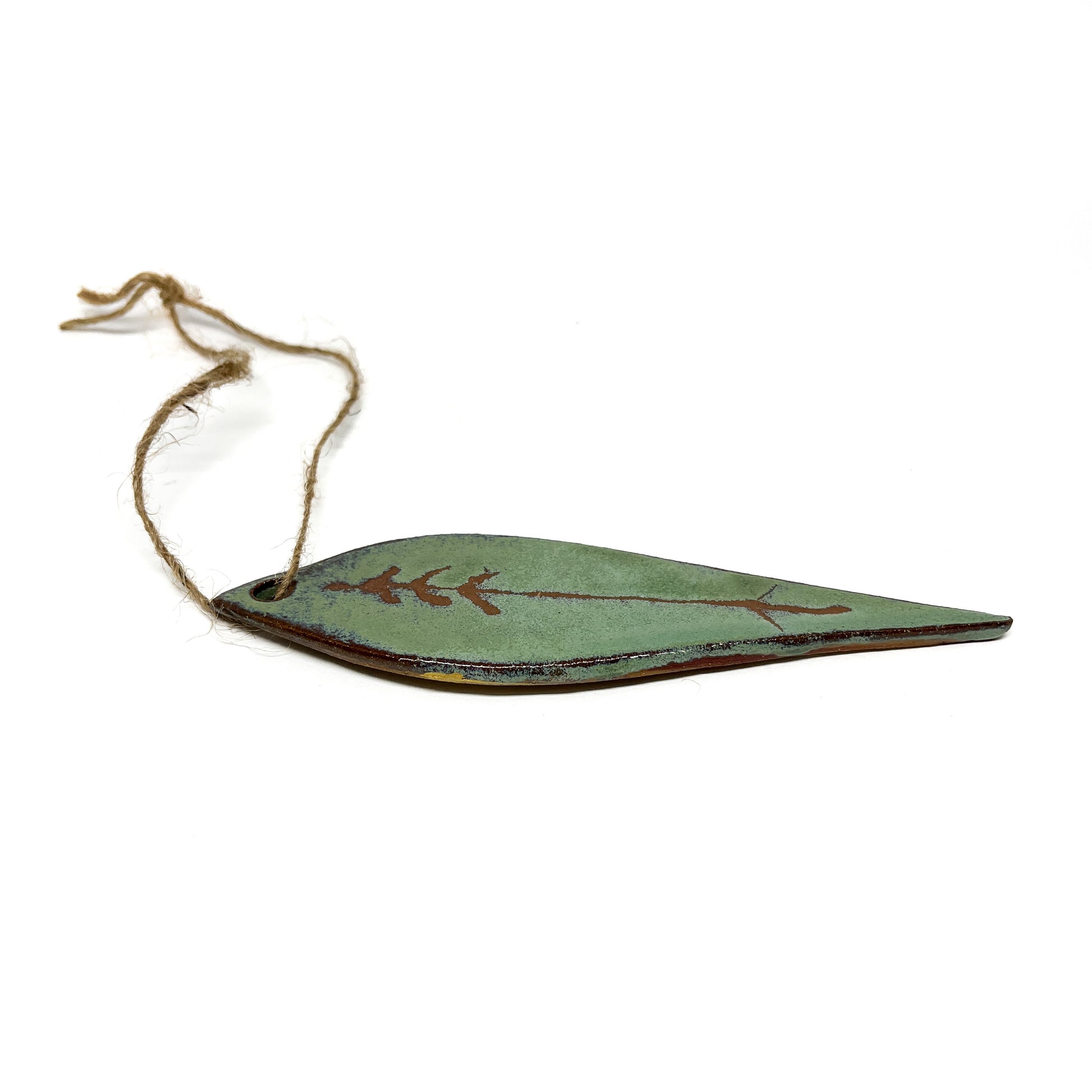 Green leaf-shaped ornament with tree design and twine, lying horizontally.