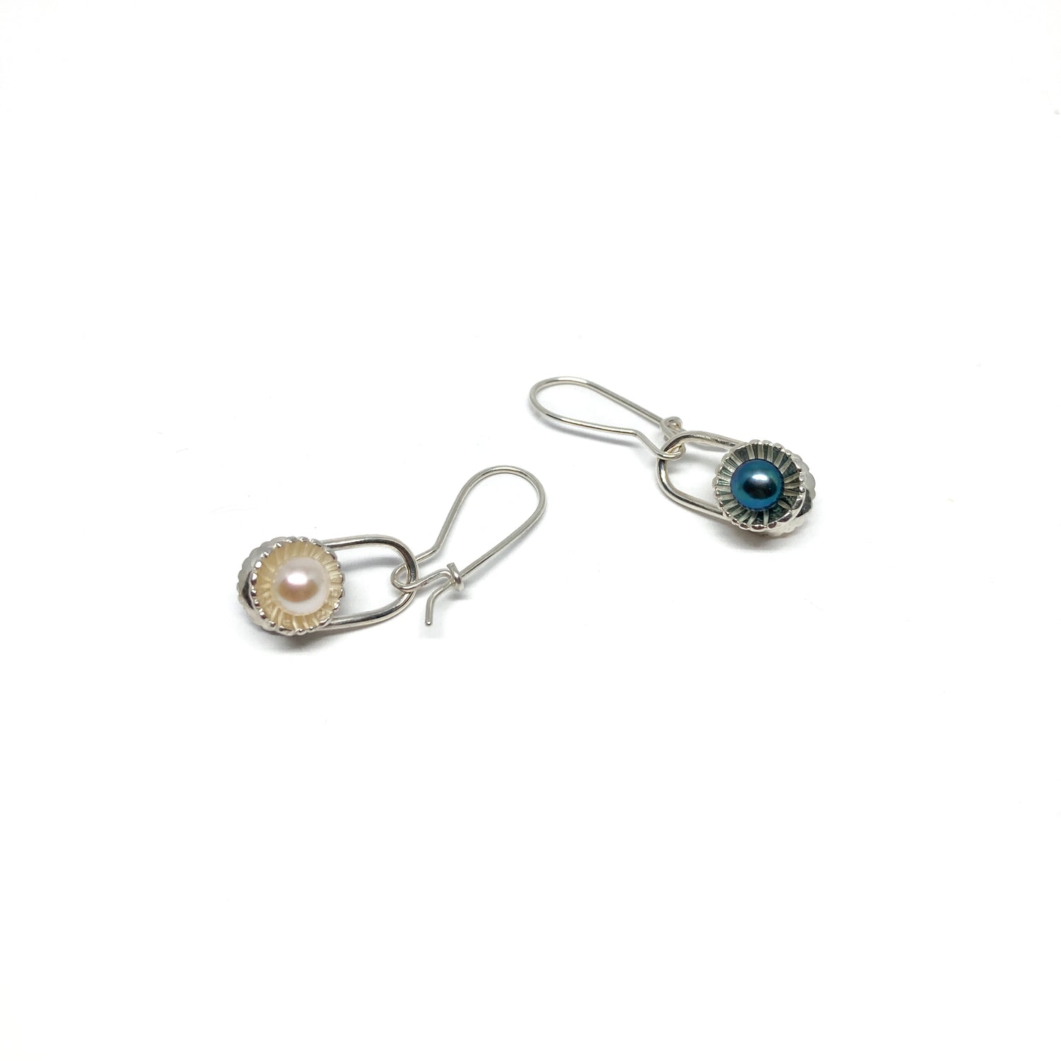 Two mismatched silver drop earrings, each with a pearl in a textured, scalloped setting.
