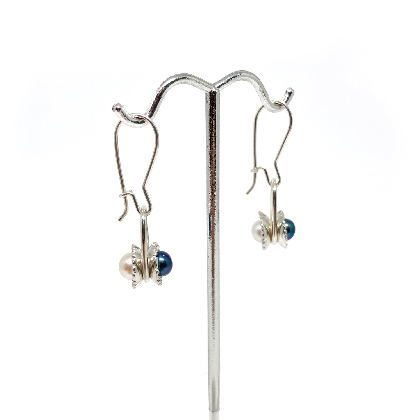 Two silver reversible slider earrings with iridescent pearls in textured, scalloped settings on a display stand.