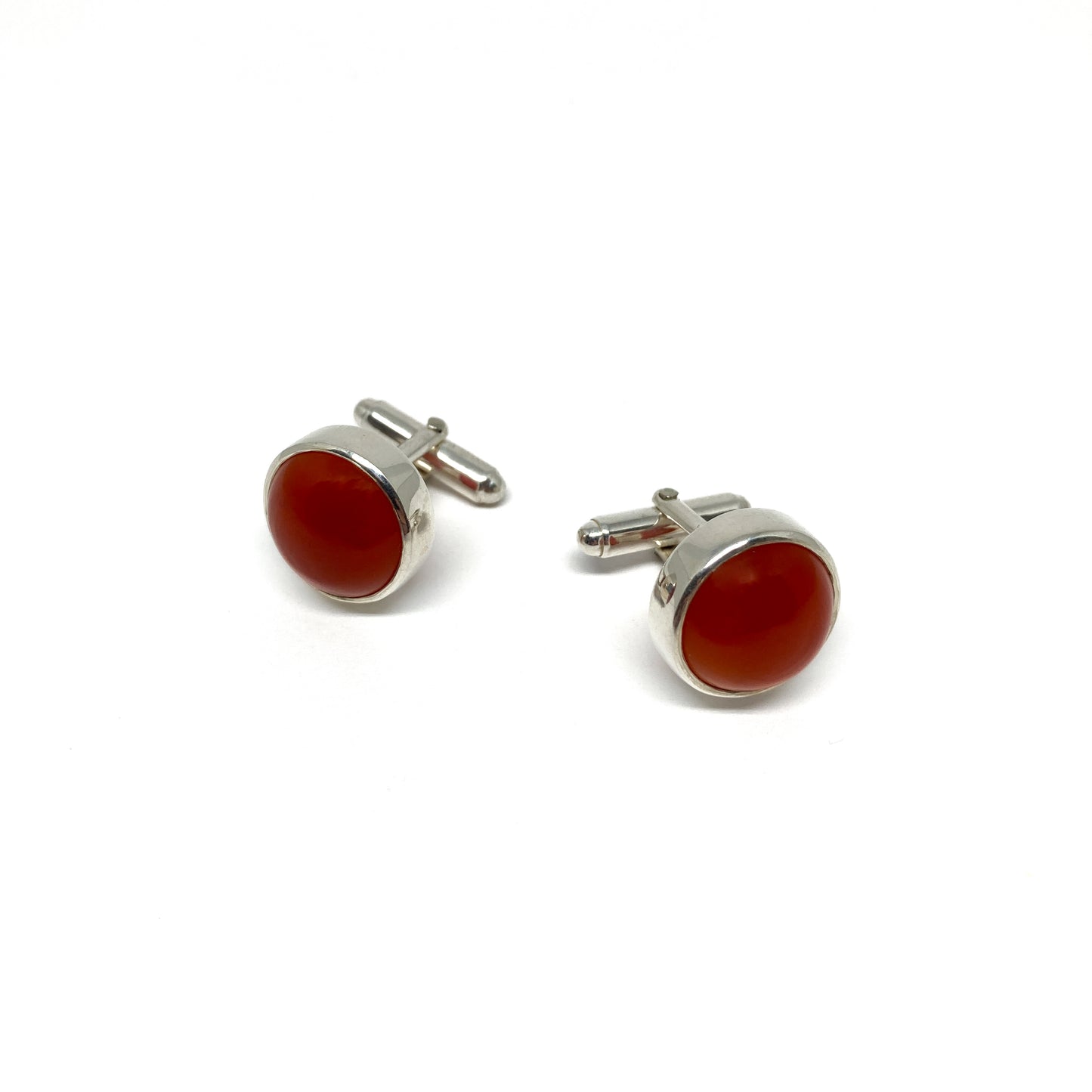 Two round silver cufflinks, each featuring a smooth, deep orange-red carnelian gemstone.