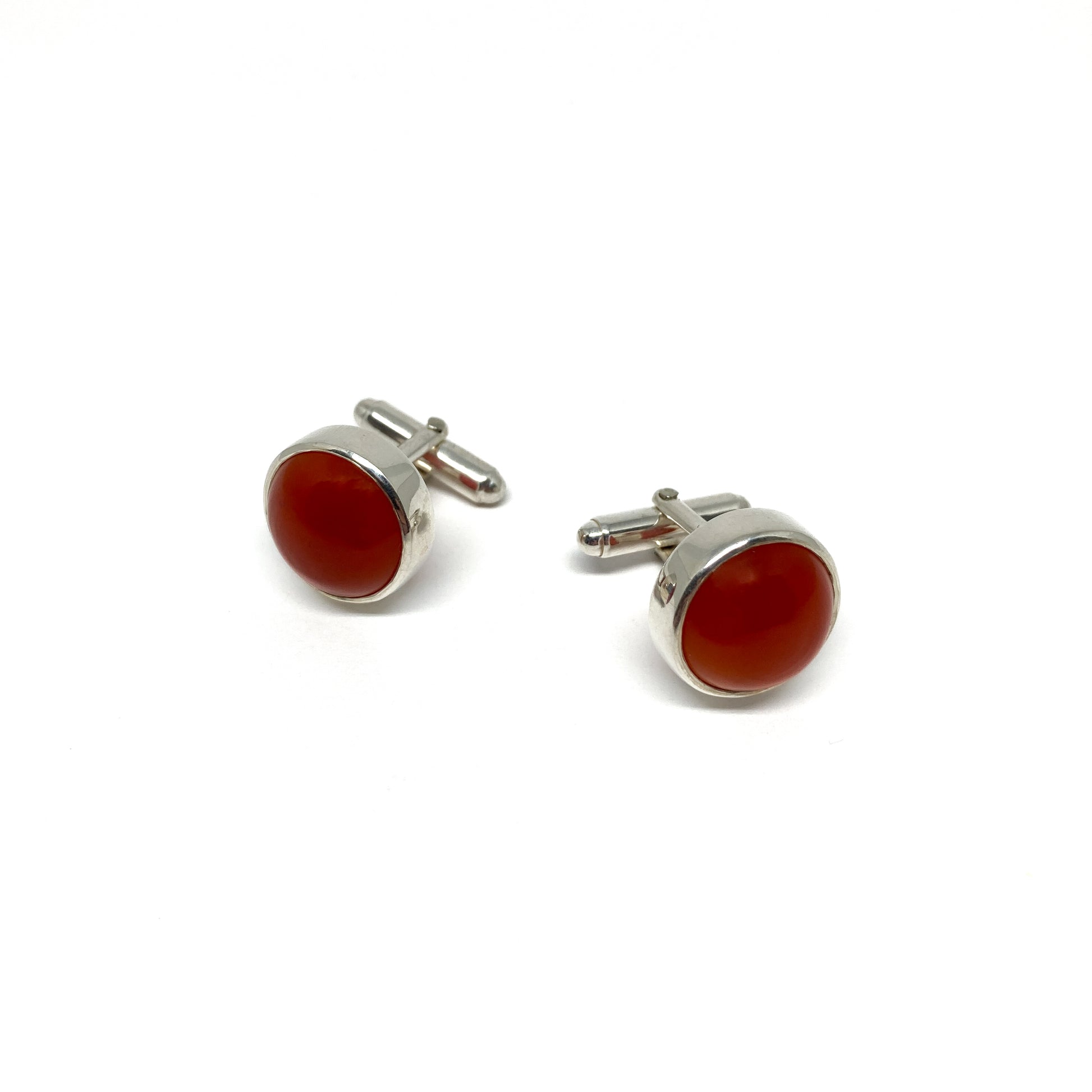 Two round silver cufflinks, each featuring a smooth, deep orange-red carnelian gemstone.