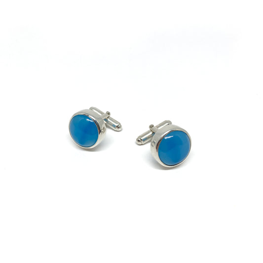 Two round silver cufflinks, each featuring a smooth, vibrant blue gemstone setting.