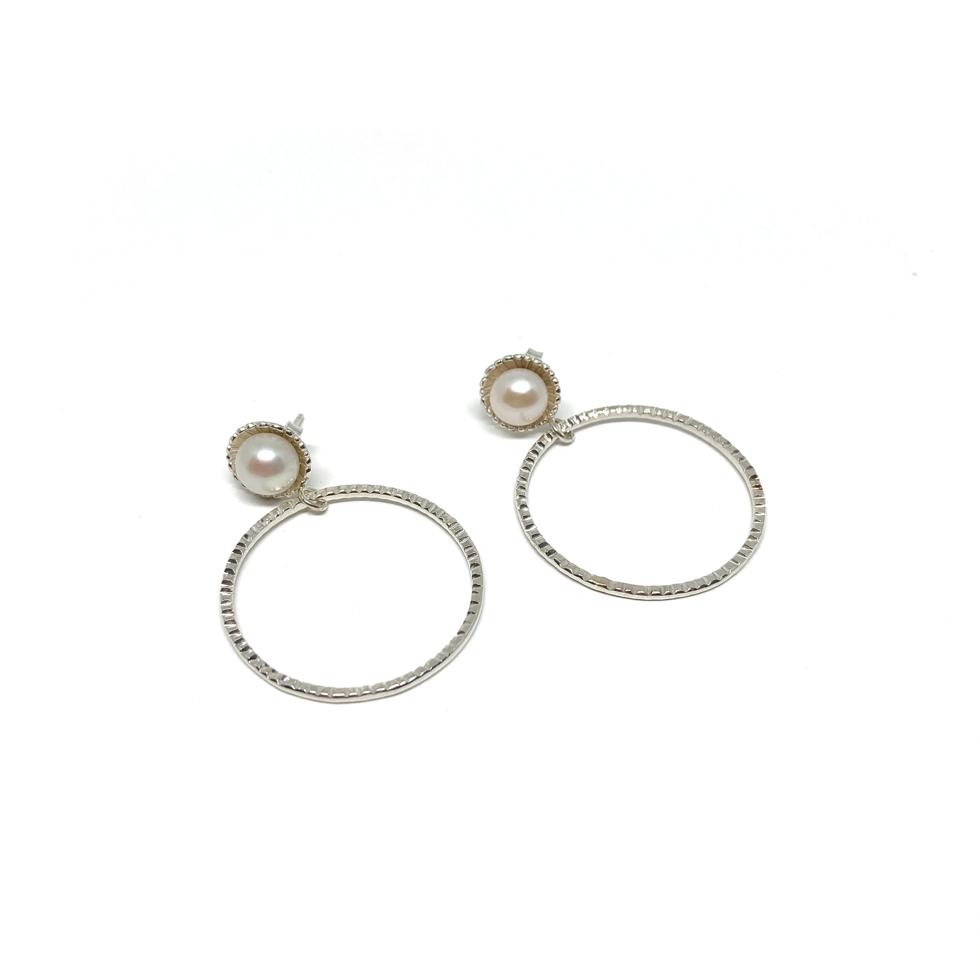 A pair of silver hoop earrings, each featuring a single white pearl set at the top of the textured hoop.