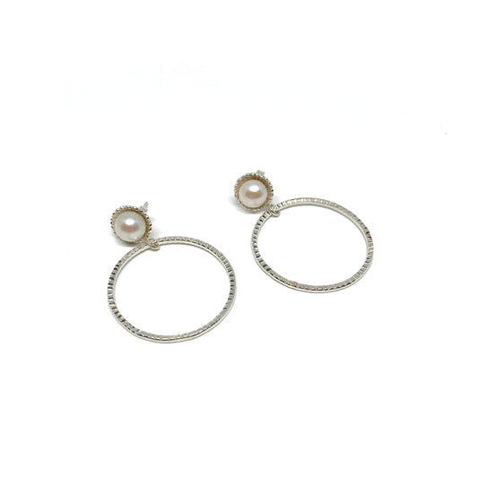 A pair of silver hoop earrings, each featuring a single white pearl set at the top of the textured hoop.