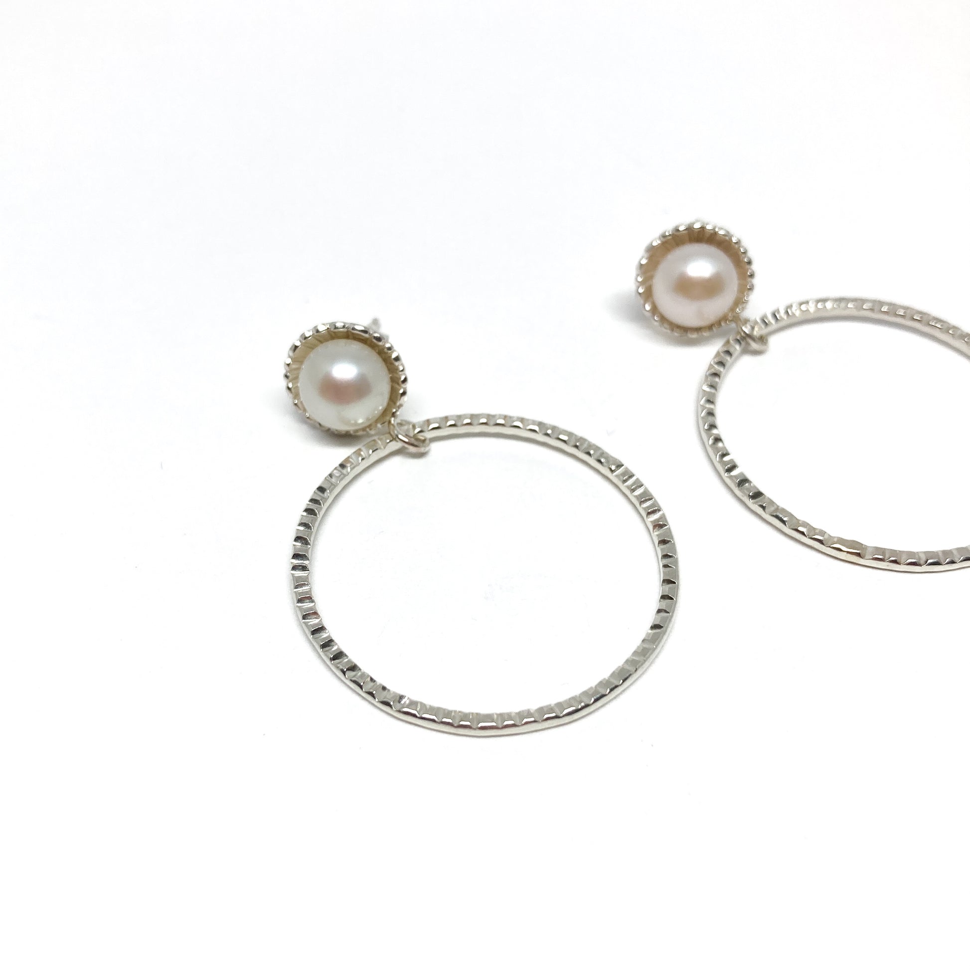 A pair of silver hoop earrings, each featuring a luminous white pearl.