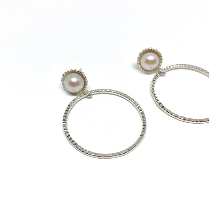 A pair of silver hoop earrings, each featuring a luminous white pearl.