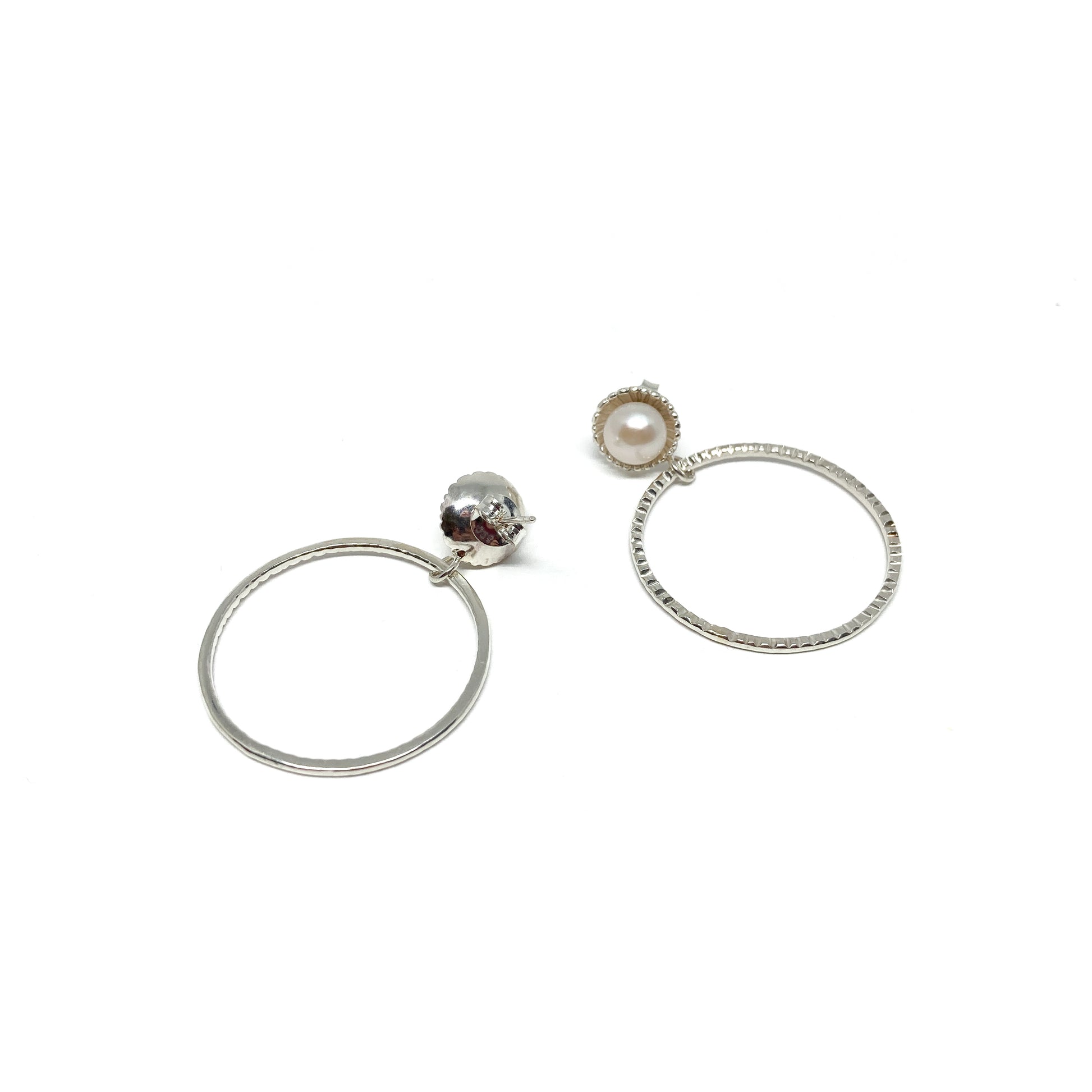 A pair of mismatched silver hoop earrings. One has a white pearl, the other a carved skull with red accents.
