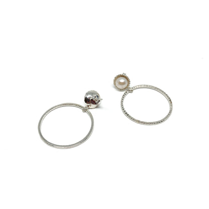 A pair of mismatched silver hoop earrings. One has a white pearl, the other a carved skull with red accents.