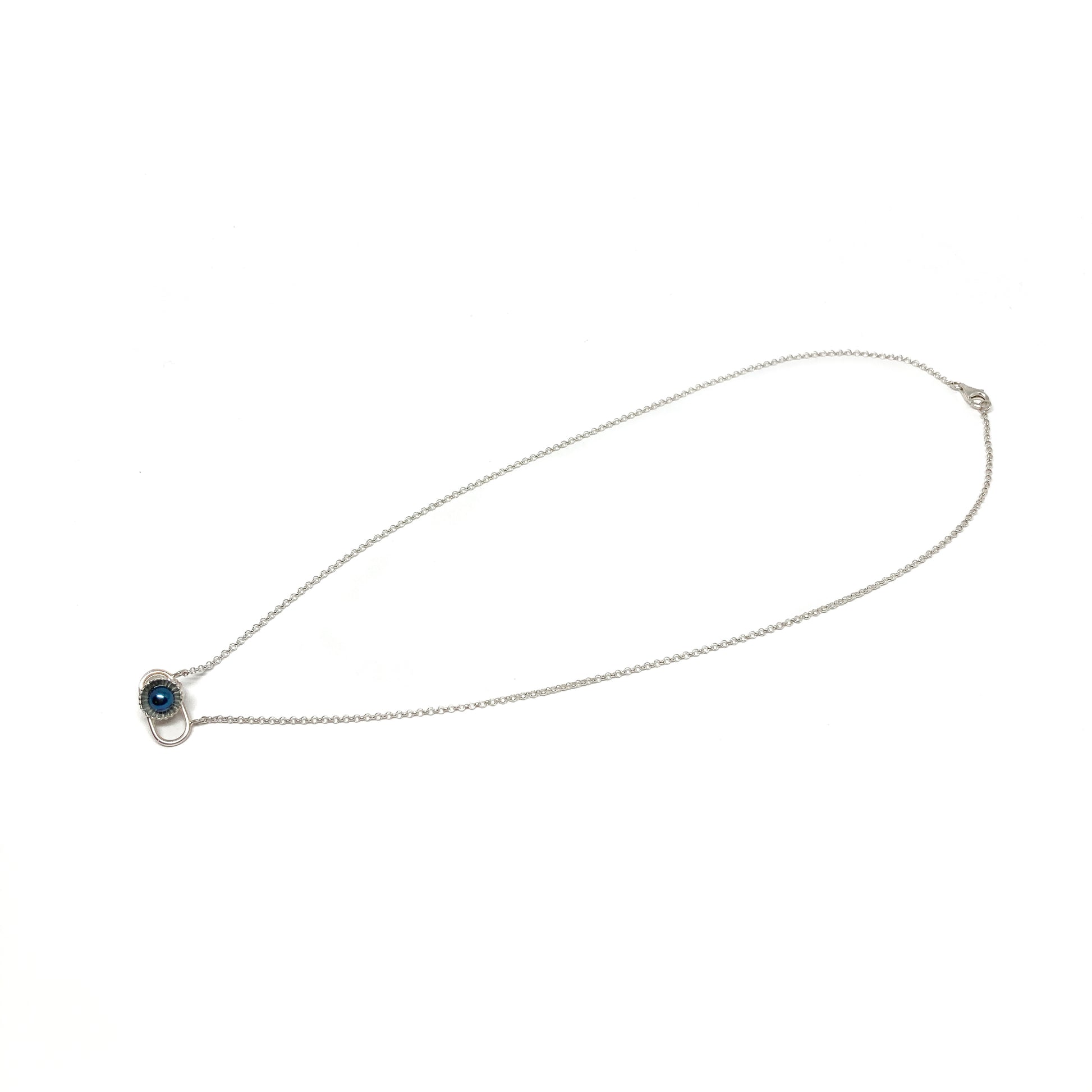 A delicate silver necklace with a small pendant featuring a dark, iridescent Taku Poe pearl in a textured setting.