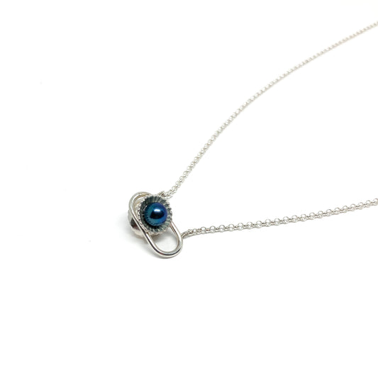 A silver necklace featuring a dark, iridescent Taku Poe pearl encased in a textured setting, attached to a delicate chain.
