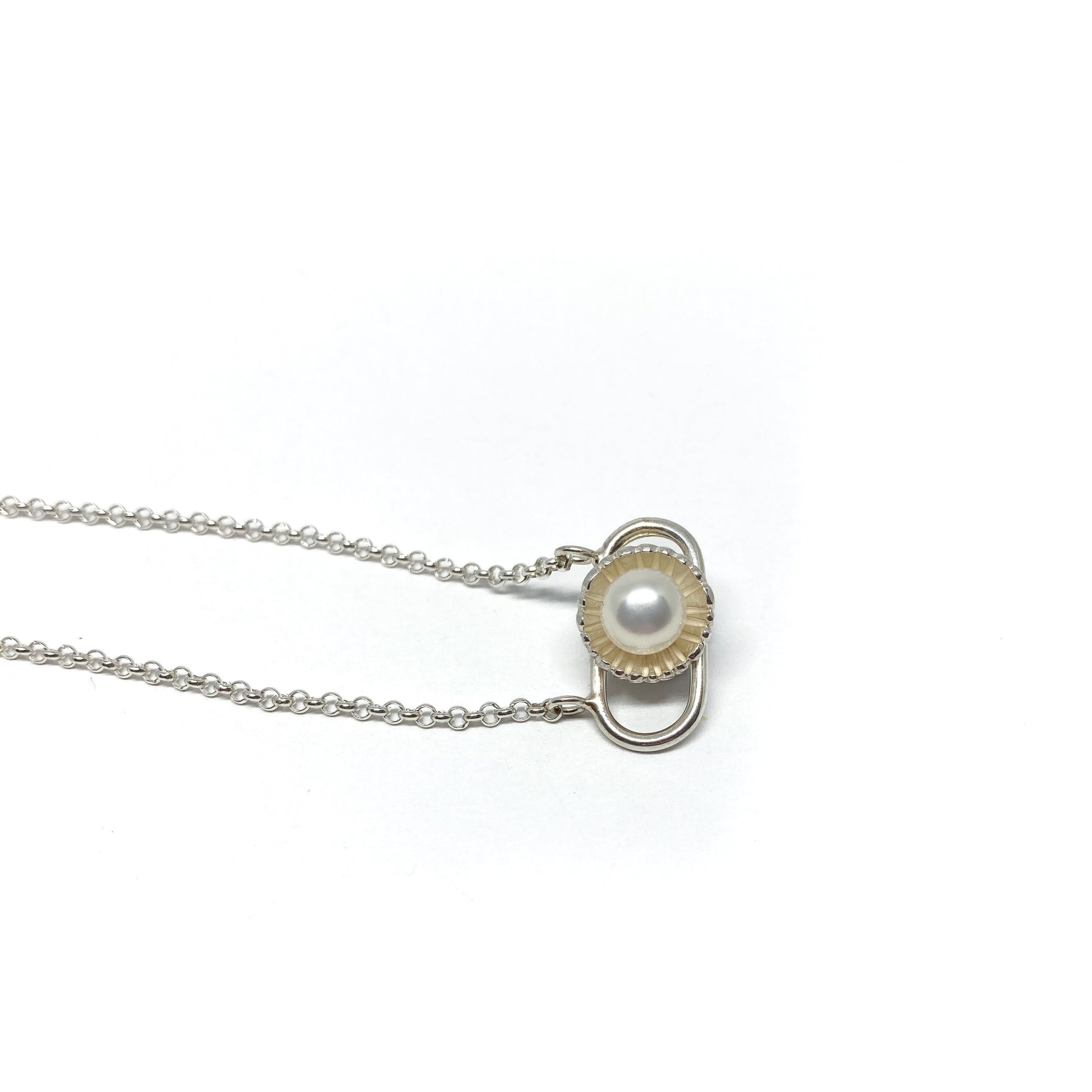 A silver necklace with a pendant featuring a single white pearl set in a textured, stylized circular and bar design.
