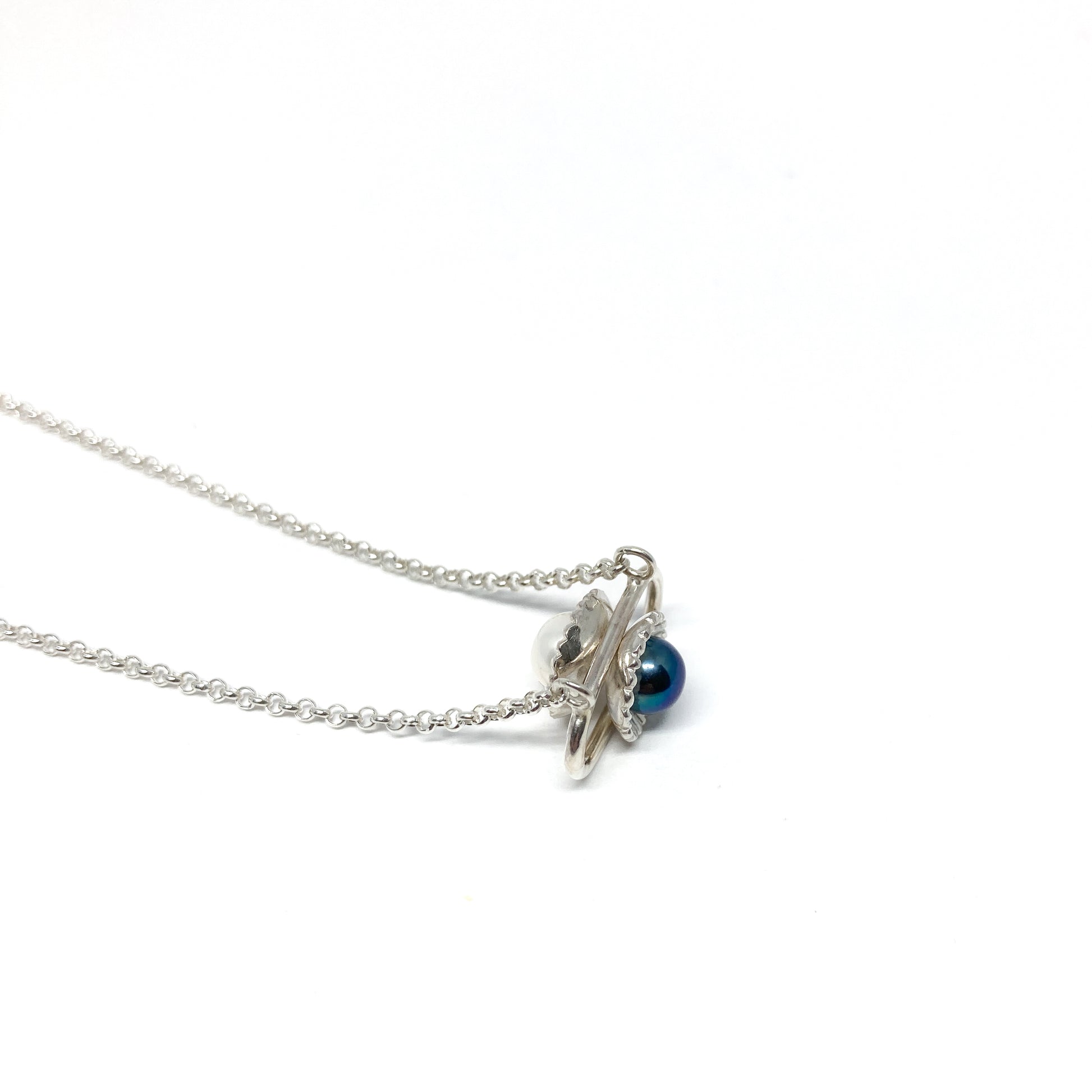 A silver necklace with a pendant featuring a dark, iridescent Taku Poe pearl and a smaller white pearl in a stylized setting.