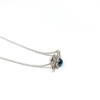 A silver necklace with a pendant featuring a dark, iridescent Taku Poe pearl and a smaller white pearl in a stylized setting.