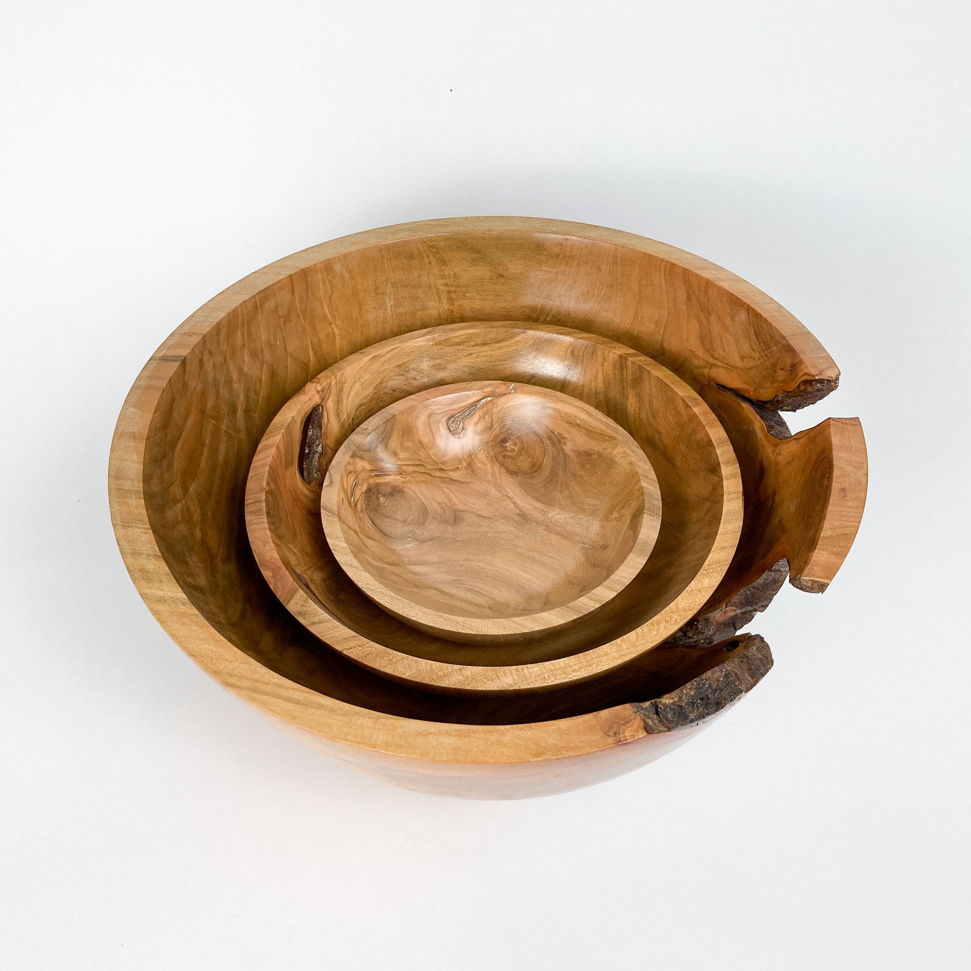 Three wooden bowls nested inside each other, showing natural wood grain and a piece of bark on the largest bowl.