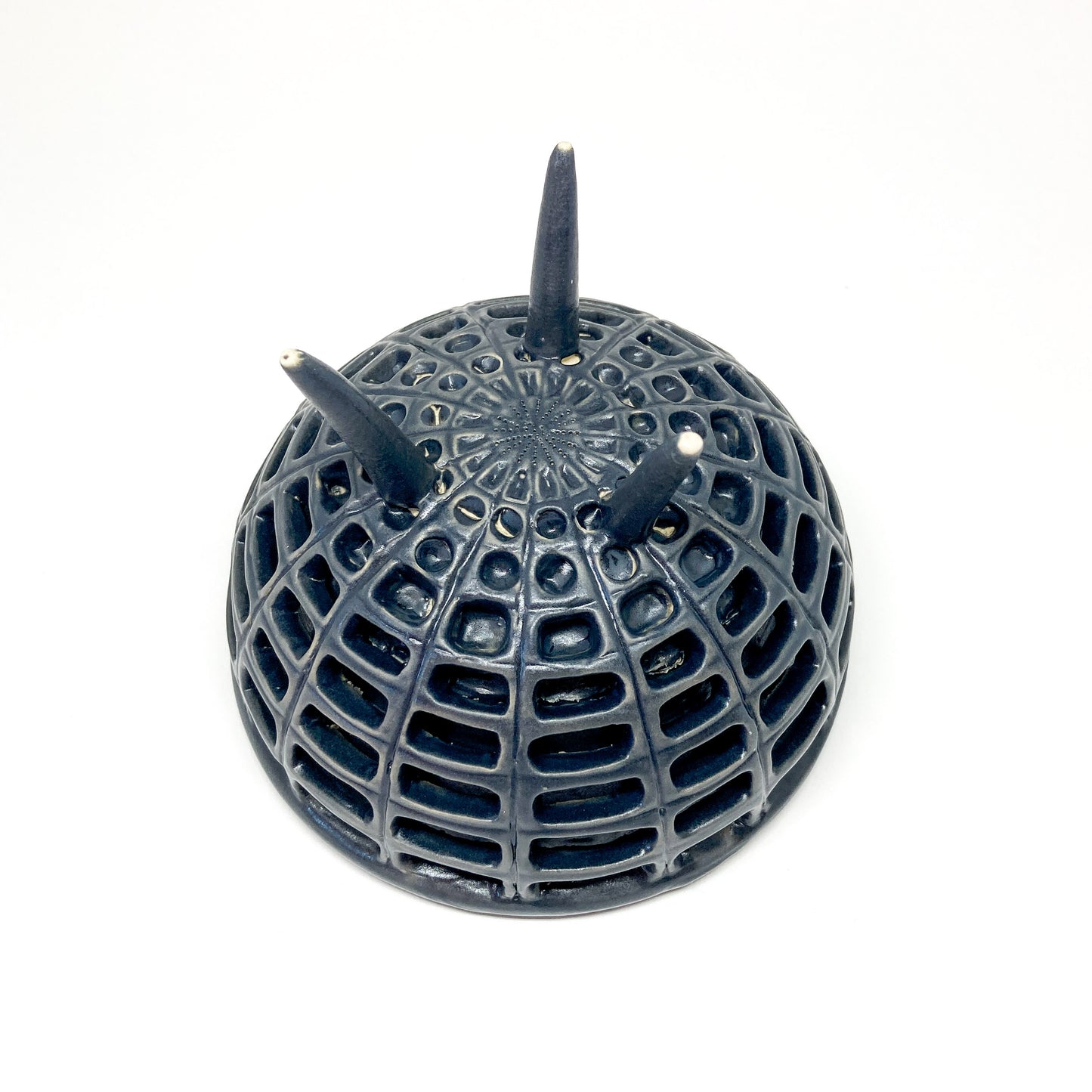 Bottom view of a black, double-walled diatom bowl revealing its intricate lattice structure and the tips of its three legs.