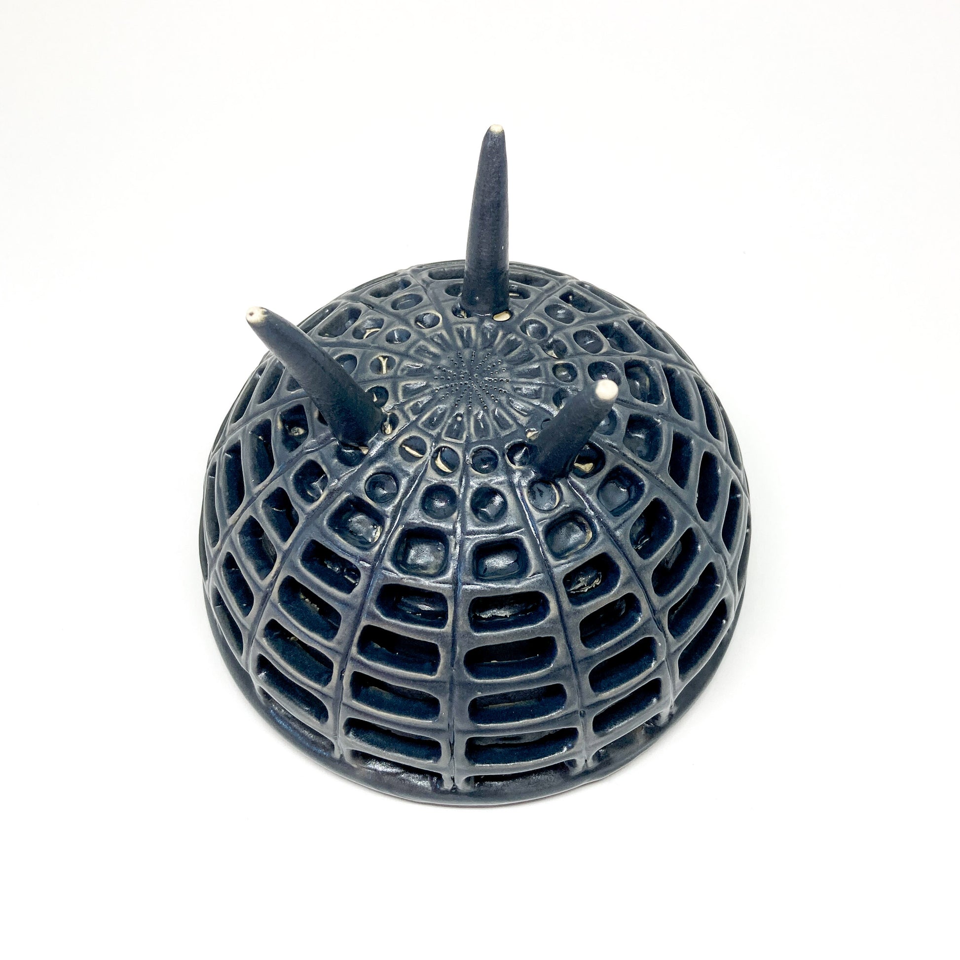 Bottom view of a black, double-walled diatom bowl revealing its intricate lattice structure and the tips of its three legs.