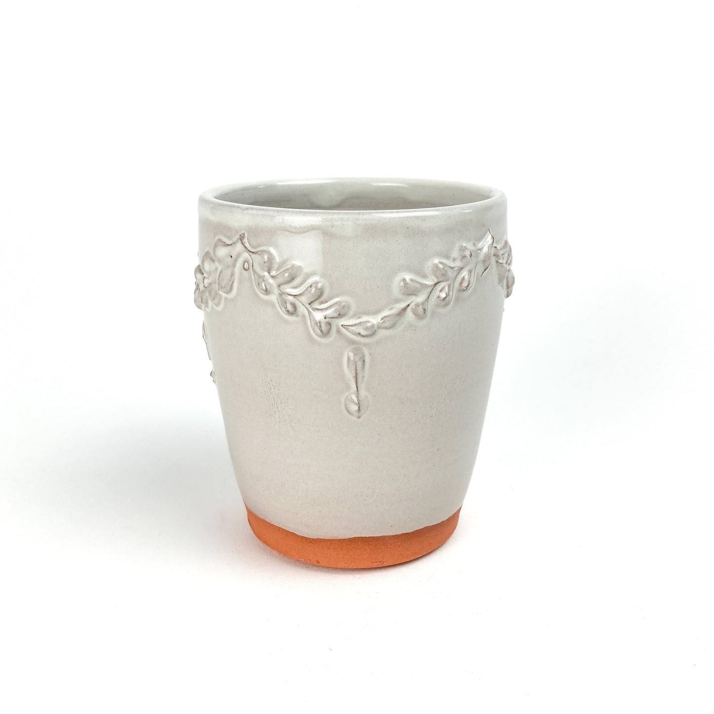 Ceramic tumbler with a raised coral and garland design around the upper portion and a visible unglazed base.