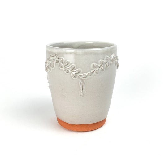 Ceramic tumbler with a raised coral and garland design around the upper portion and a visible unglazed base.