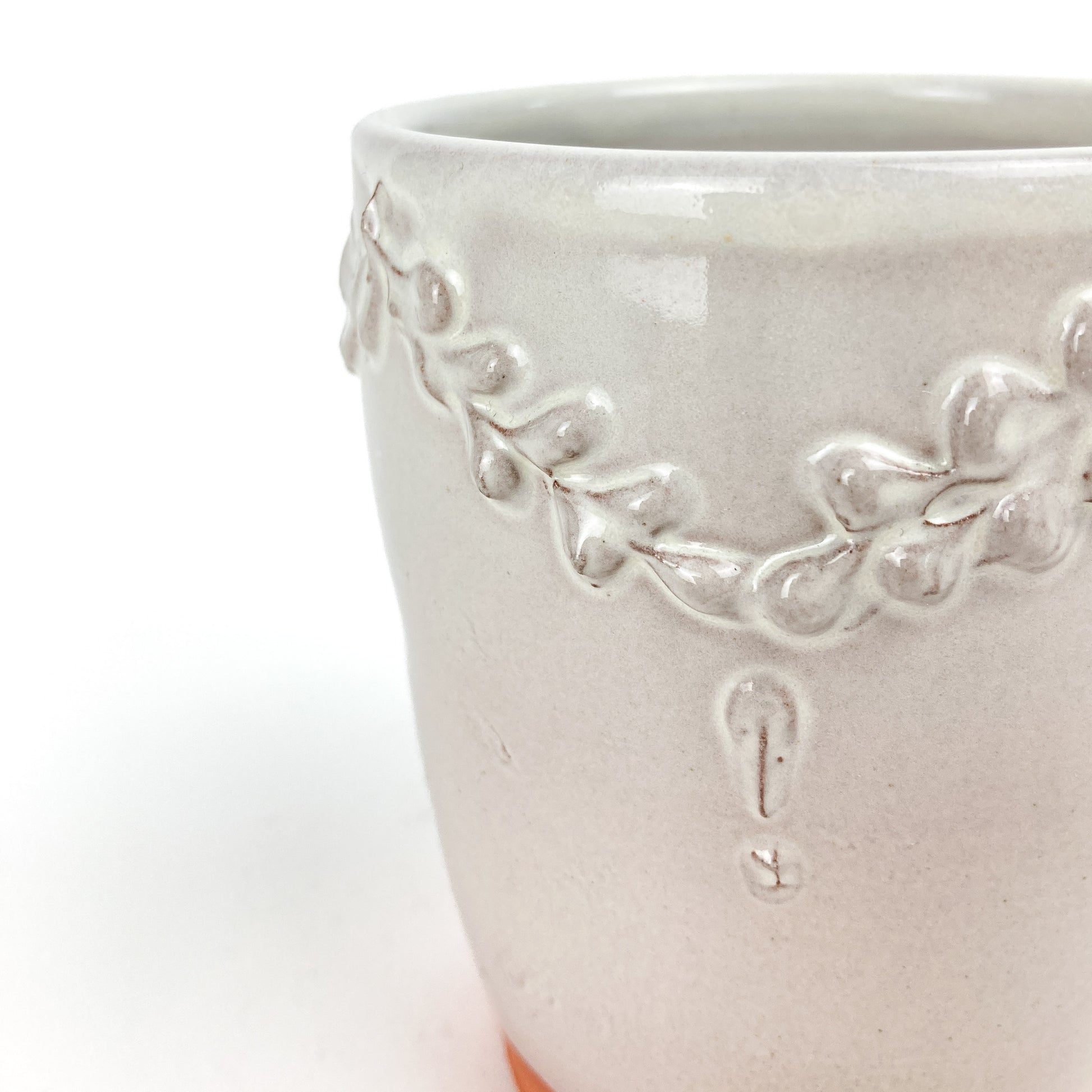 Close-up of a ceramic tumbler showing the raised coral and garland decoration and textured surface.