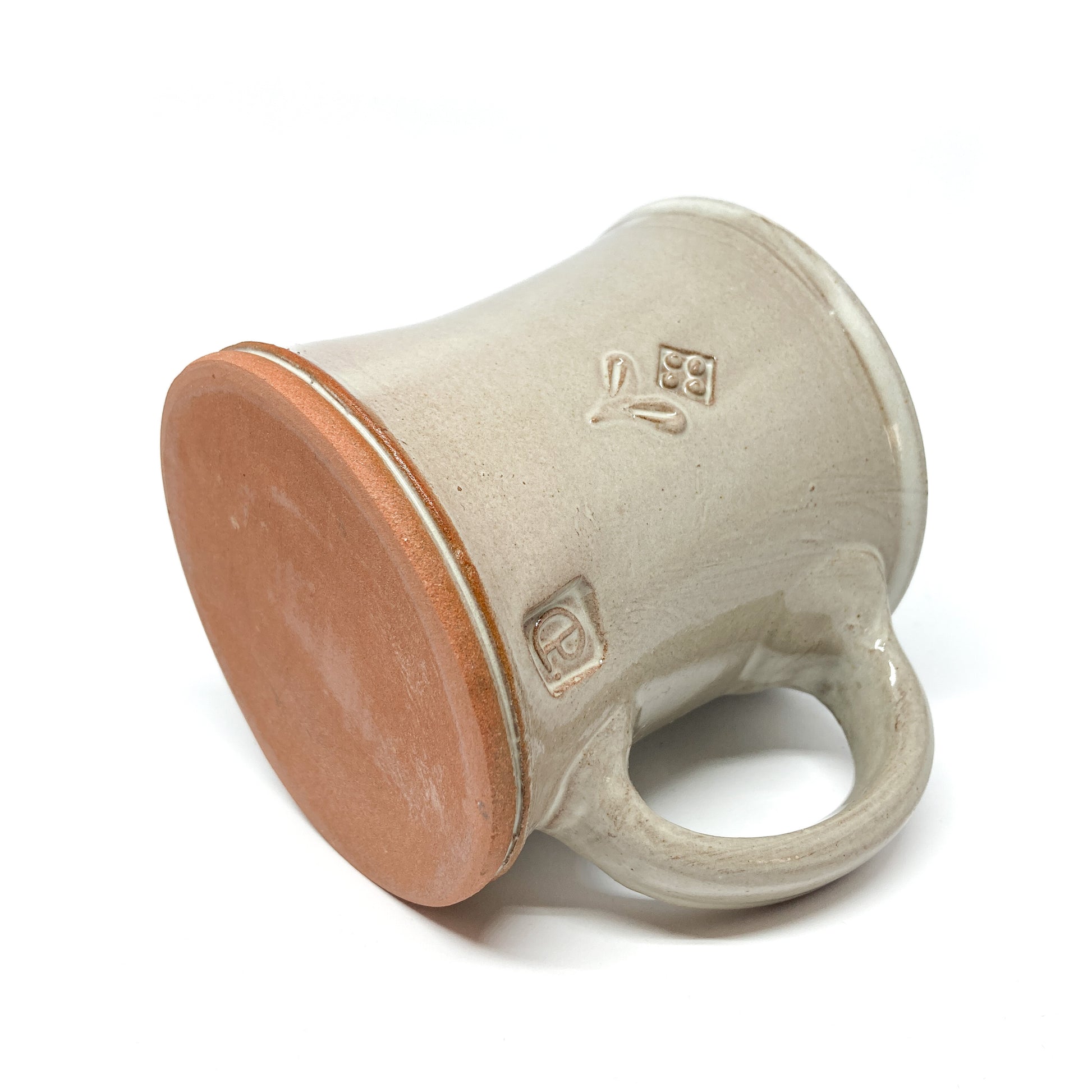 Angled view of a speckled, glazed ceramic mug showing the textured base and embossed designs.
