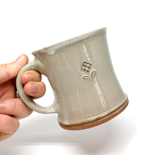 Hand holds a speckled, glazed ceramic mug with a small, embossed floral design.