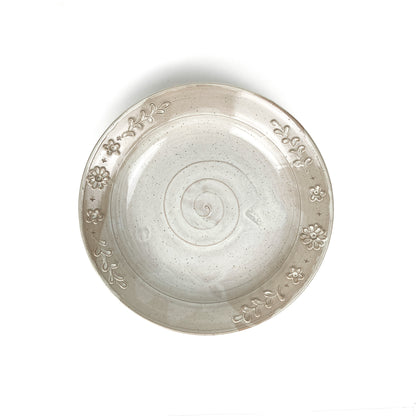 Overhead view of a speckled, glazed ceramic plate with a spiral center and embossed floral and leaf border.